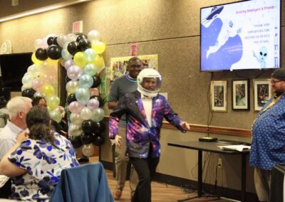 Elliot dressed as a flamboyant astronaut entering the dining room with Jeremy in a demure, sensible outfit following him