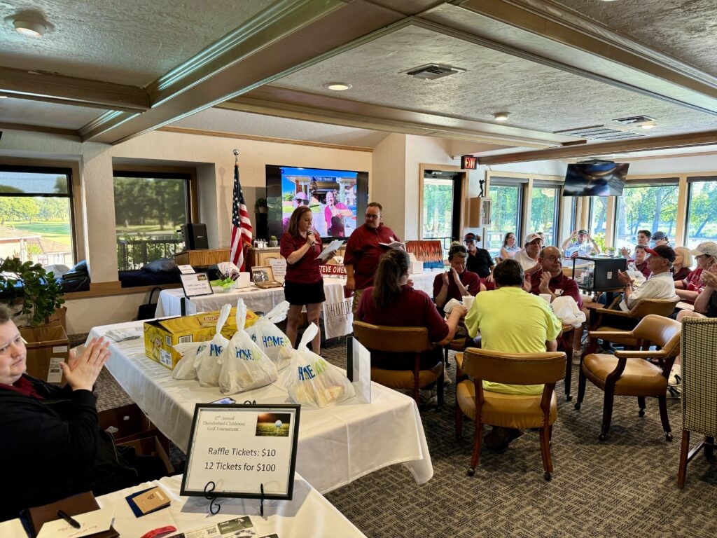 A stately dining room of a country club with a speaker in front of an audience.